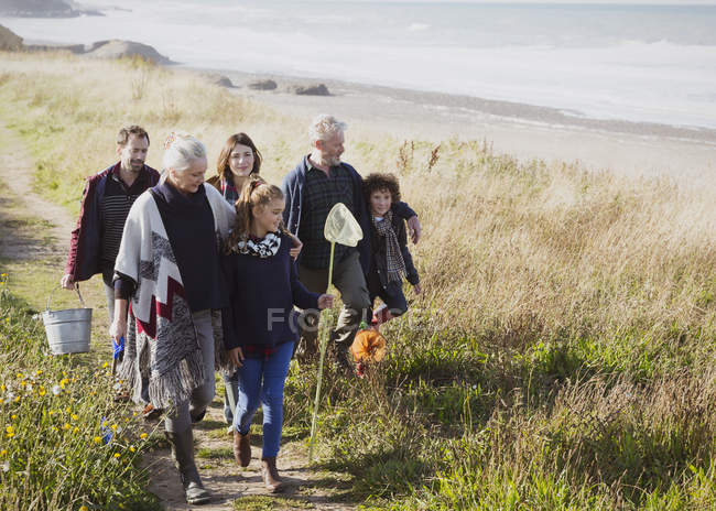 Multi-generation family walking with nets and bucket on sunny grass beach path — Stock Photo