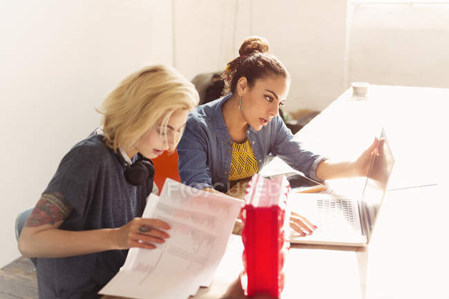 Jeunes femmes d'affaires créatives avec ordinateur portable et paperasserie au bureau — Photo de stock