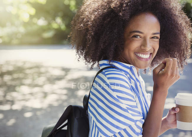 Portrait enthusiastic woman with afro drinking coffee in park — Stock Photo