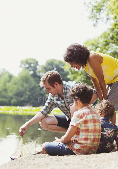 Family playing with toy sailboat at lakeside — Stock Photo