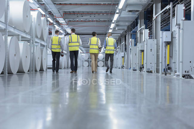 Arbeiter in reflektierender Kleidung laufen an großen Papierspulen in der Druckerei vorbei — Stockfoto