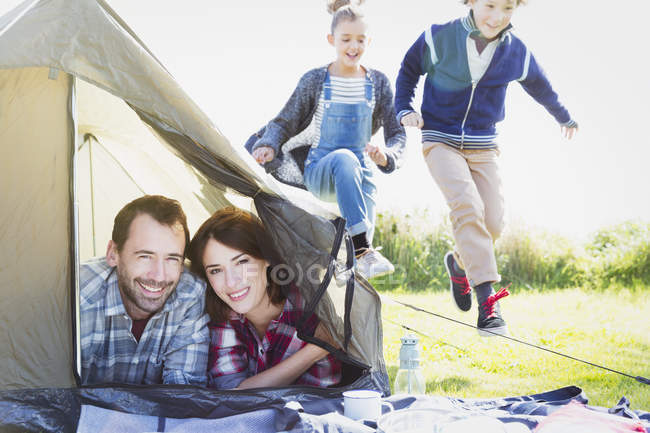 Портрет улыбающейся пары в палатке с детьми, играющими поблизости — стоковое фото