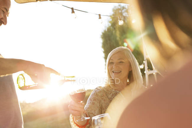 Uomo anziano versando vino per moglie sul patio soleggiato — Foto stock