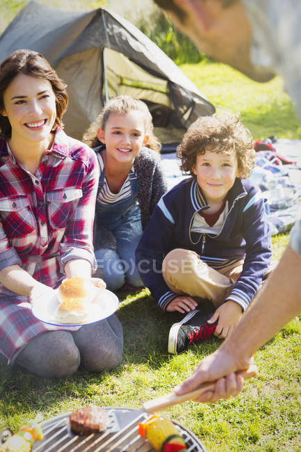 Familia viendo padre barbacoa en la parrilla del camping - foto de stock