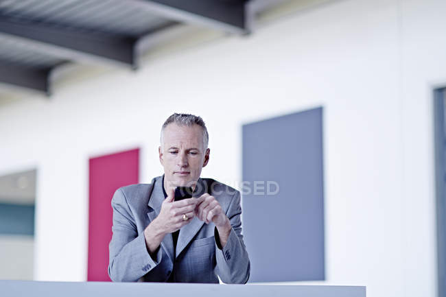 Успішний дорослий бізнесмен, використовуючи мобільний телефон у вестибюлі — стокове фото