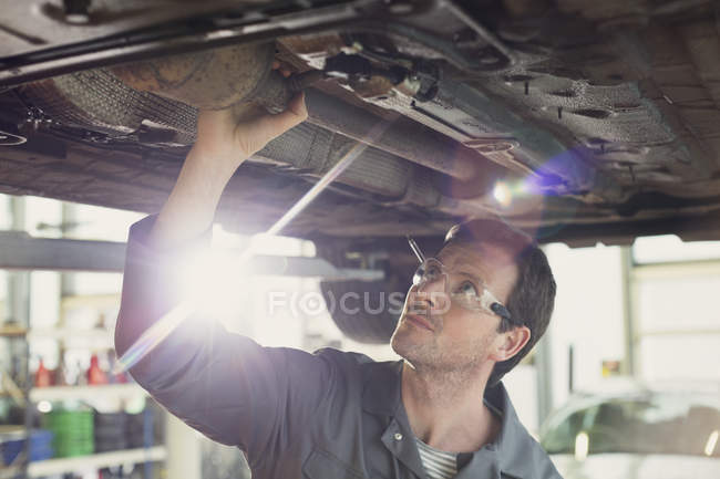 Mécanicien travaillant sous voiture dans un atelier de réparation automobile — Photo de stock