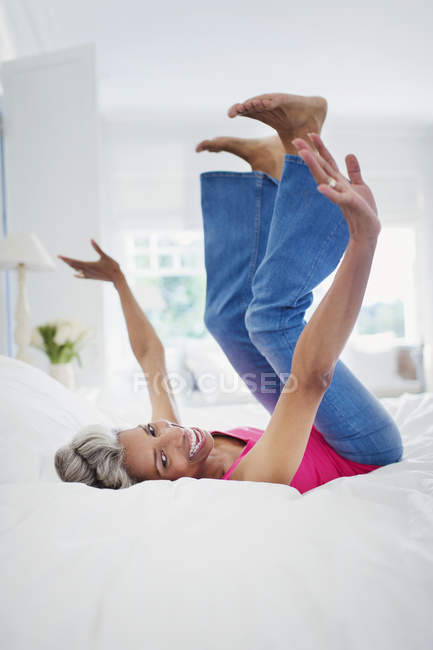 Portrait playful mature woman falling onto bed — Stock Photo