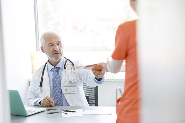 Doctor at desk giving medical record to nurse in doctor?s office — Stock Photo