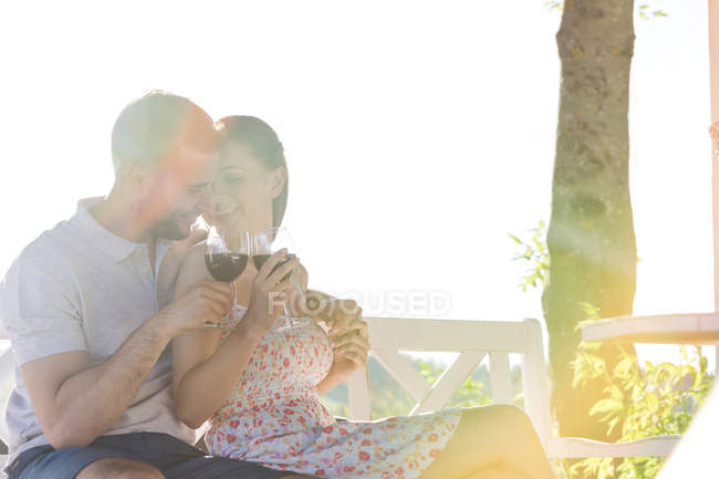 Affettuosa coppia che abbraccia e beve vino rosso sulla panchina soleggiata — Foto stock