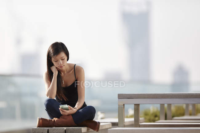 Mujer mensajes de texto en el banco al aire libre - foto de stock