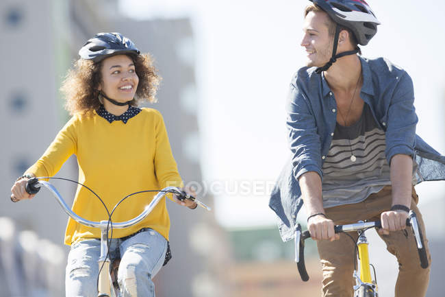 Young couple with helmets riding bicycles in city — Stock Photo