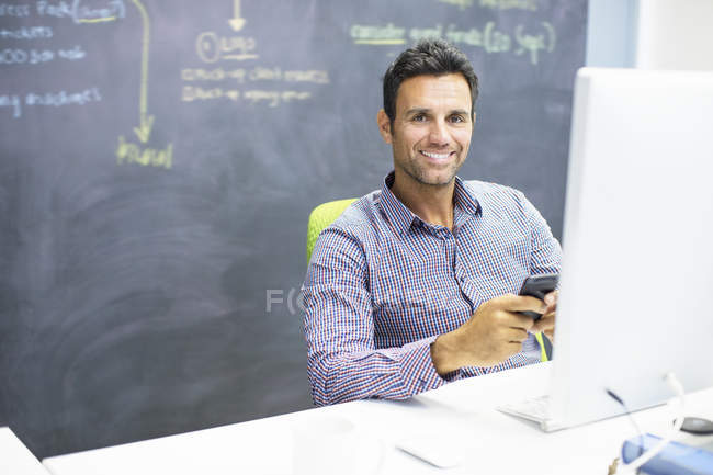 Businessman using cell phone at desk in office — Stock Photo