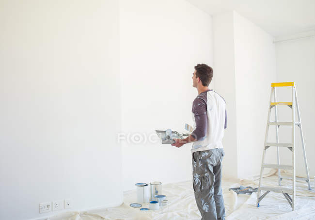 Homem com bandeja de tinta olhando para a parede branca — Fotografia de Stock