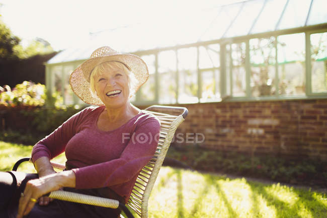 Porträt begeisterte Seniorin sitzt vor sonnigem Gewächshaus — Stockfoto