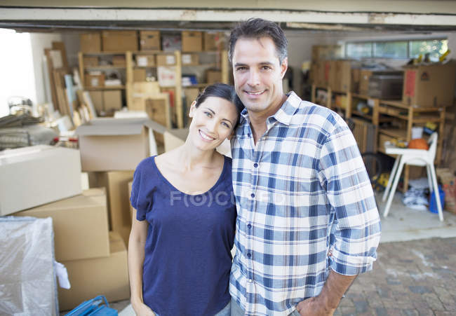 Portrait of smiling couple outside garage among cardboard boxes — Stock Photo