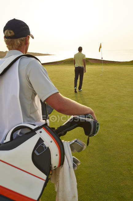 Rear view of golfer and caddy nearing golf flag — Stock Photo
