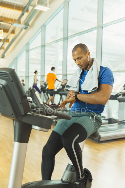 Man checking smart watch on exercise bike at gym — Stock Photo
