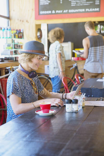 Mujer con sombrero usando tableta digital en la cafetería - foto de stock
