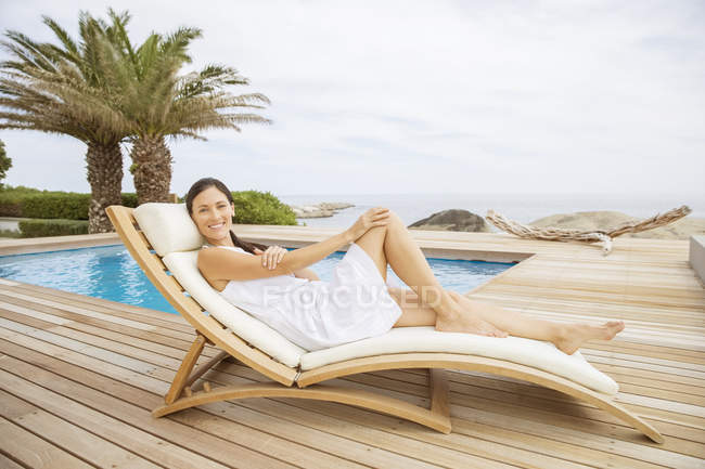 Mujer relajante en silla de salón en la piscina - foto de stock