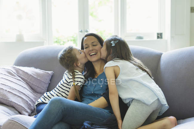 Filles embrassant les joues de la mère sur le canapé du salon — Photo de stock