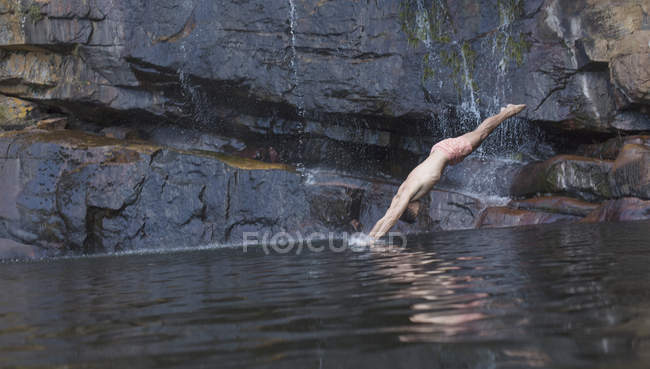 Человек ныряет в озеро против камня — стоковое фото