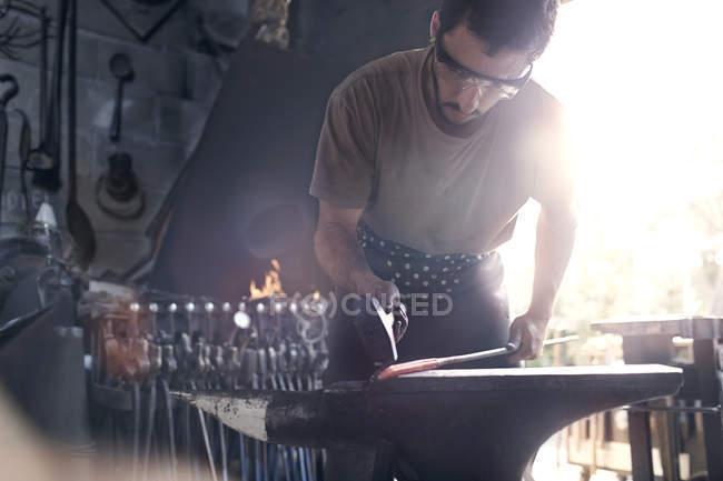 Herrero forjando hierro caliente en yunque en forja - foto de stock