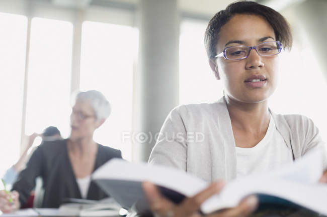 Mujer seria leyendo libro en aula de educación de adultos - foto de stock