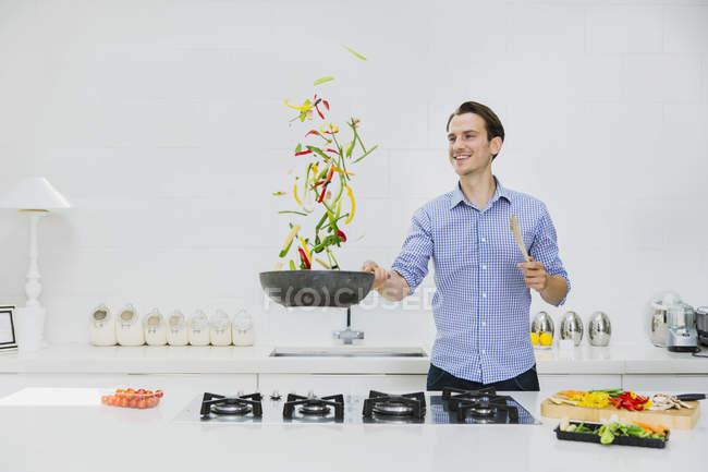 Lächelnder Mann blättert Gemüse in Pfanne in Küche — Stockfoto
