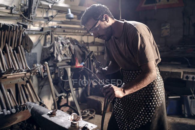 Blacksmith heating metal with blowtorch in forge — Stock Photo