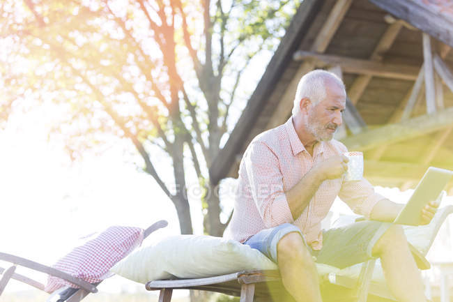Hombre mayor beber café y el uso de tabletas digitales en el sillón en el patio trasero - foto de stock