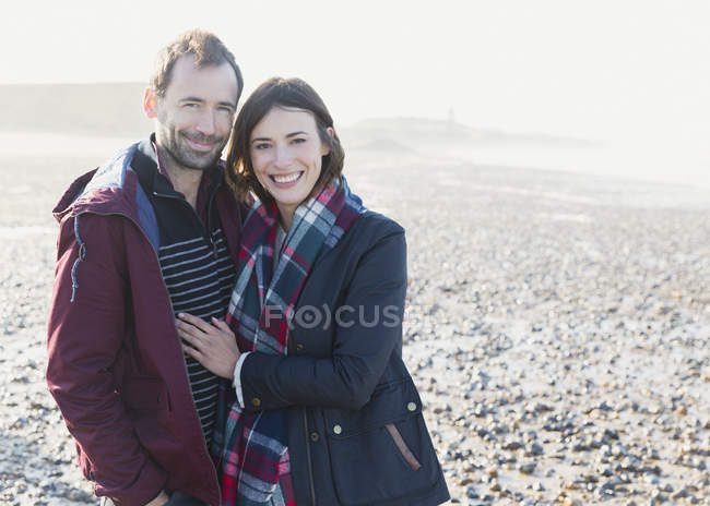Porträt lächelndes Paar, das sich am sonnigen felsigen Strand umarmt — Stockfoto