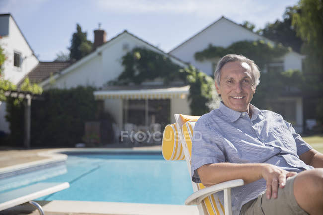 Hombre sonriente en silla de salón junto a la piscina - foto de stock