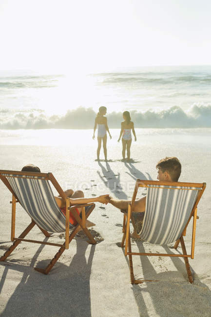 Батьки спостерігають за дочками на пляжі на заході сонця — стокове фото