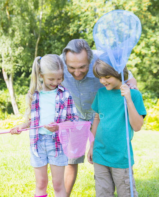 Grandfather and grandchildren looking at butterfly in net — Stock Photo