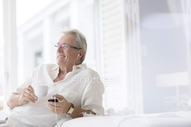 Hombre mayor escuchando auriculares en el patio - foto de stock