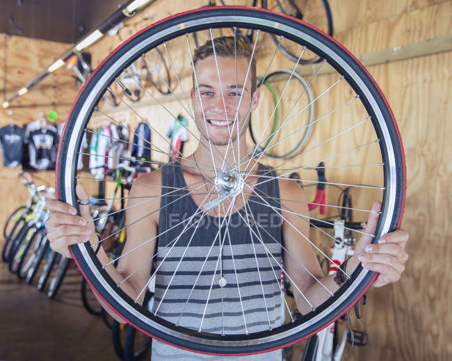 Retrato sorridente jovem segurando roda de bicicleta na loja de bicicletas — Fotografia de Stock