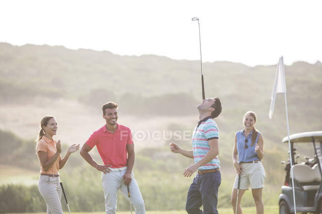 Amici guardando l'uomo equilibrio golf club sul naso — Foto stock