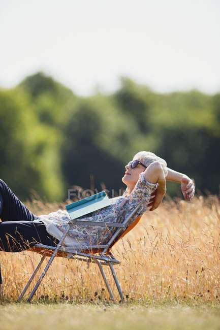 Беззаботная пожилая женщина расслабляется с книгой в солнечном поле — стоковое фото