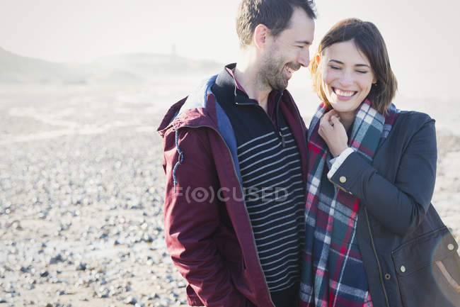 Smiling brunette couple standing on sunny rocky beach — Stock Photo