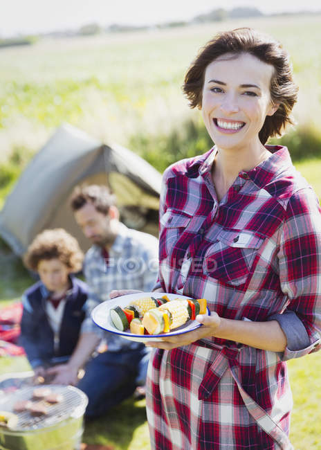 Retrato mujer sonriente con pinchos de verduras en el camping - foto de stock