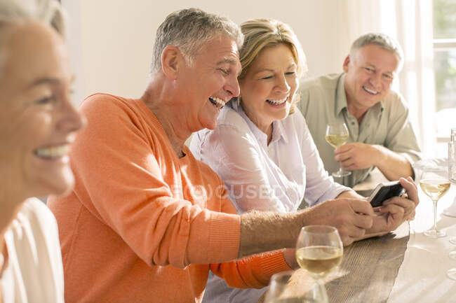 Casais seniores bebendo vinho e olhando para o telefone celular — Fotografia de Stock