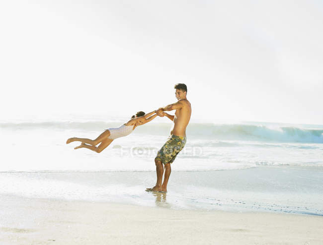 Father swinging daughter on beach — Stock Photo