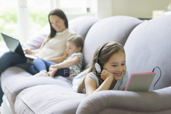 Menina com fones de ouvido e tablet digital deitado no sofá da sala de estar — Fotografia de Stock