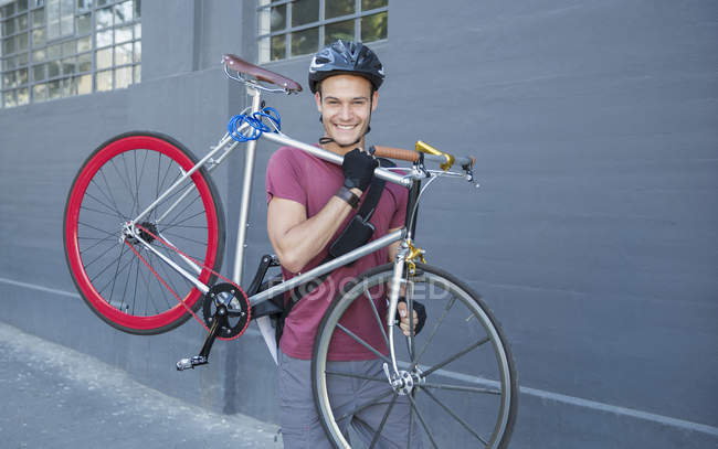 Retrato sonriente joven llevando bicicleta en la acera urbana - foto de stock