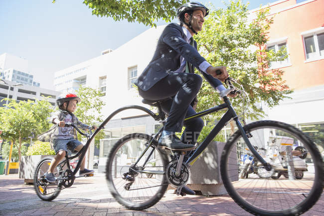 Empresario padre en traje de montar en bicicleta tándem con hijo en la acera urbana - foto de stock