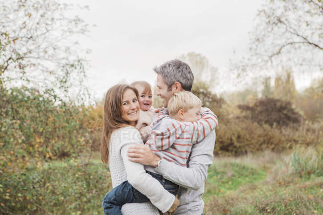 Familia sonriente abrazándose en el parque de otoño - foto de stock