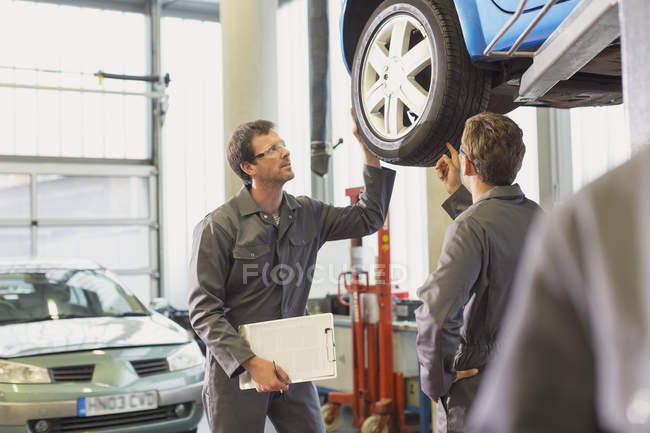 Mecánica examinando y discutiendo neumático en taller de reparación de automóviles - foto de stock