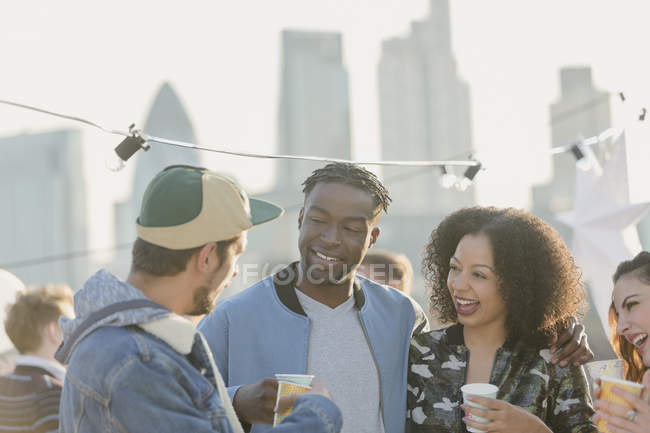 Young adult friends talking and drinking at rooftop party — Stock Photo