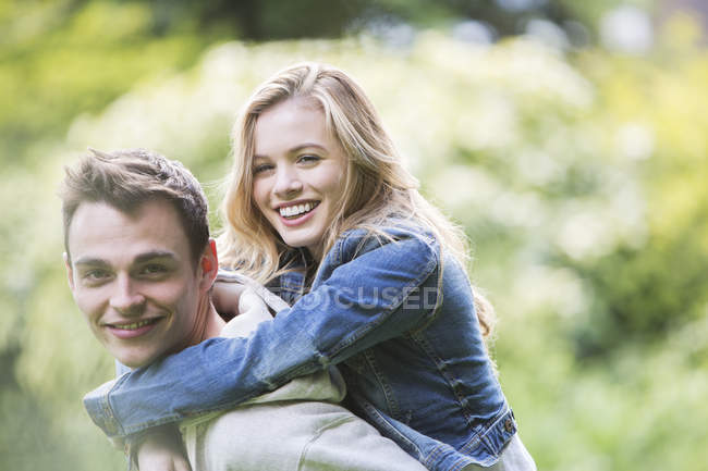 Man carrying girlfriend piggyback outdoors — Stock Photo