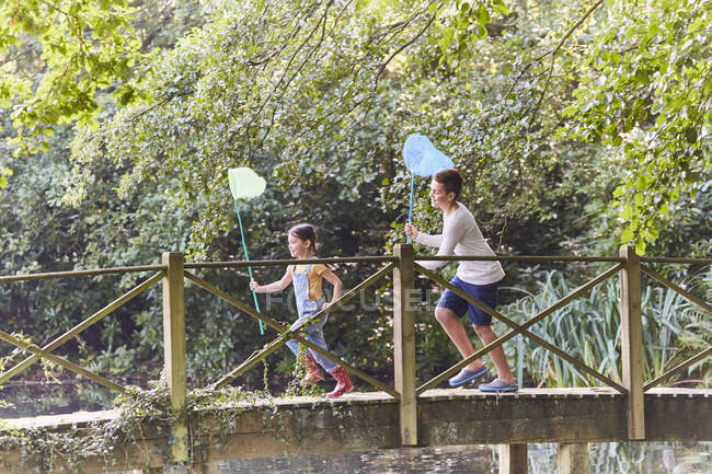 Брат и сестра бегут с бабочками по мосту в парке — стоковое фото